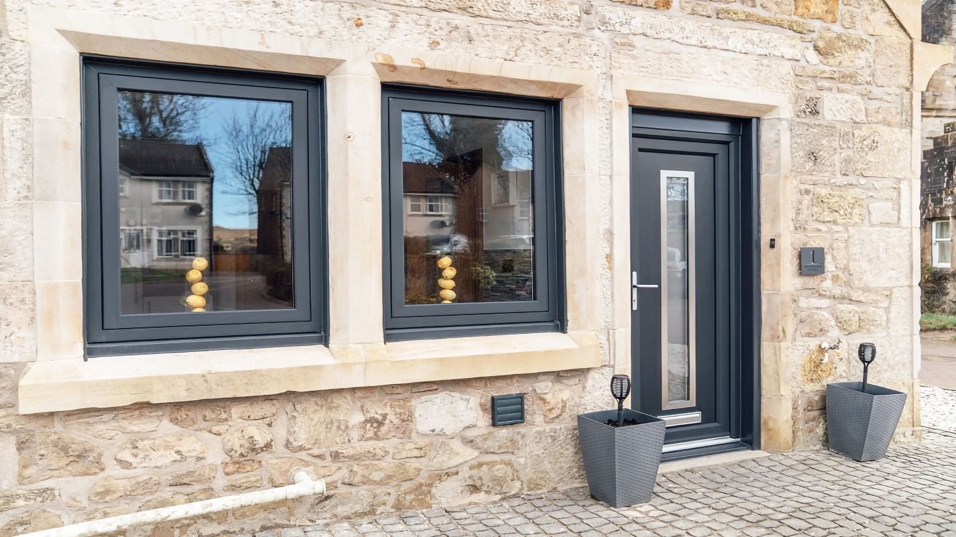 Modern flush sash Cambridge windows and a dark composite front door on a stone house.
