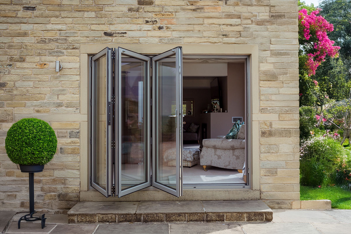 Open aluminium bifold doors leading from a stone exterior wall into a cosy living room.