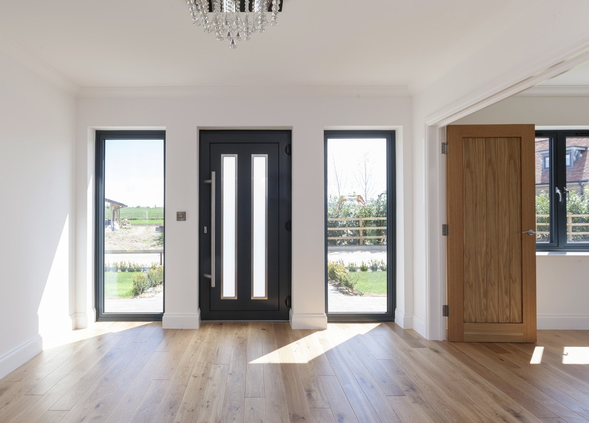 Modern black aluminium front door with vertical glass panels, flanked by full-height side windows.