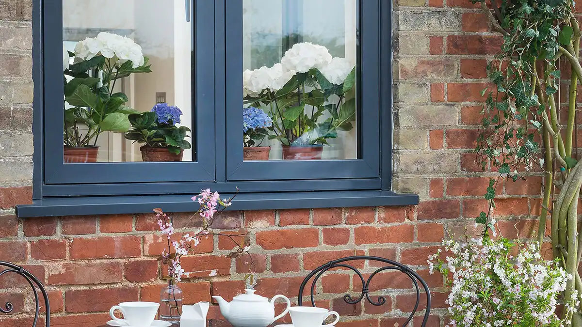Anthracite grey double glazed window on a red brick wall with potted flowers inside.