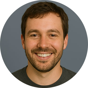 Smiling man with a beard and dark hair against a neutral grey background.