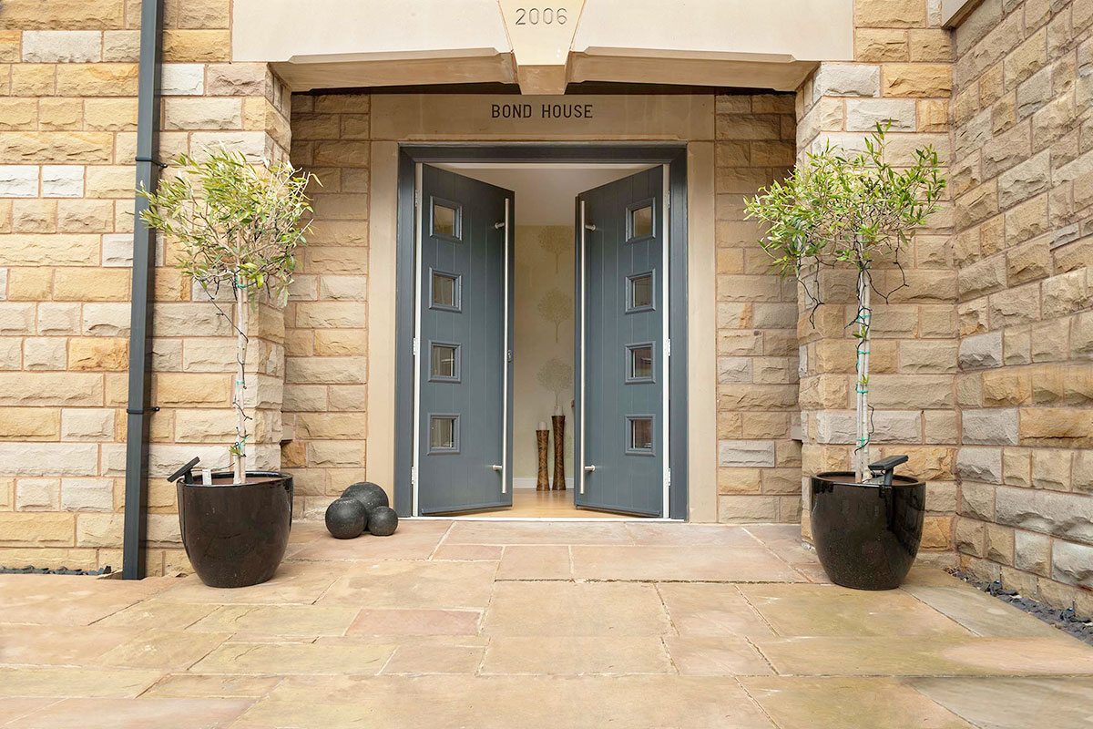 Modern grey composite double doors open at the entrance of a stone house.