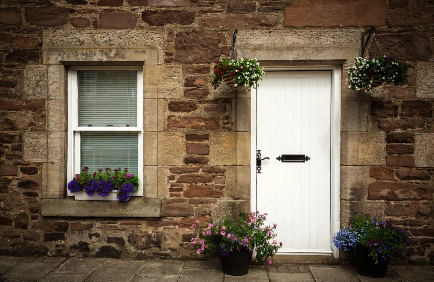 Traditional stone cottage with white wooden door and sash window decorated with hanging flower baskets