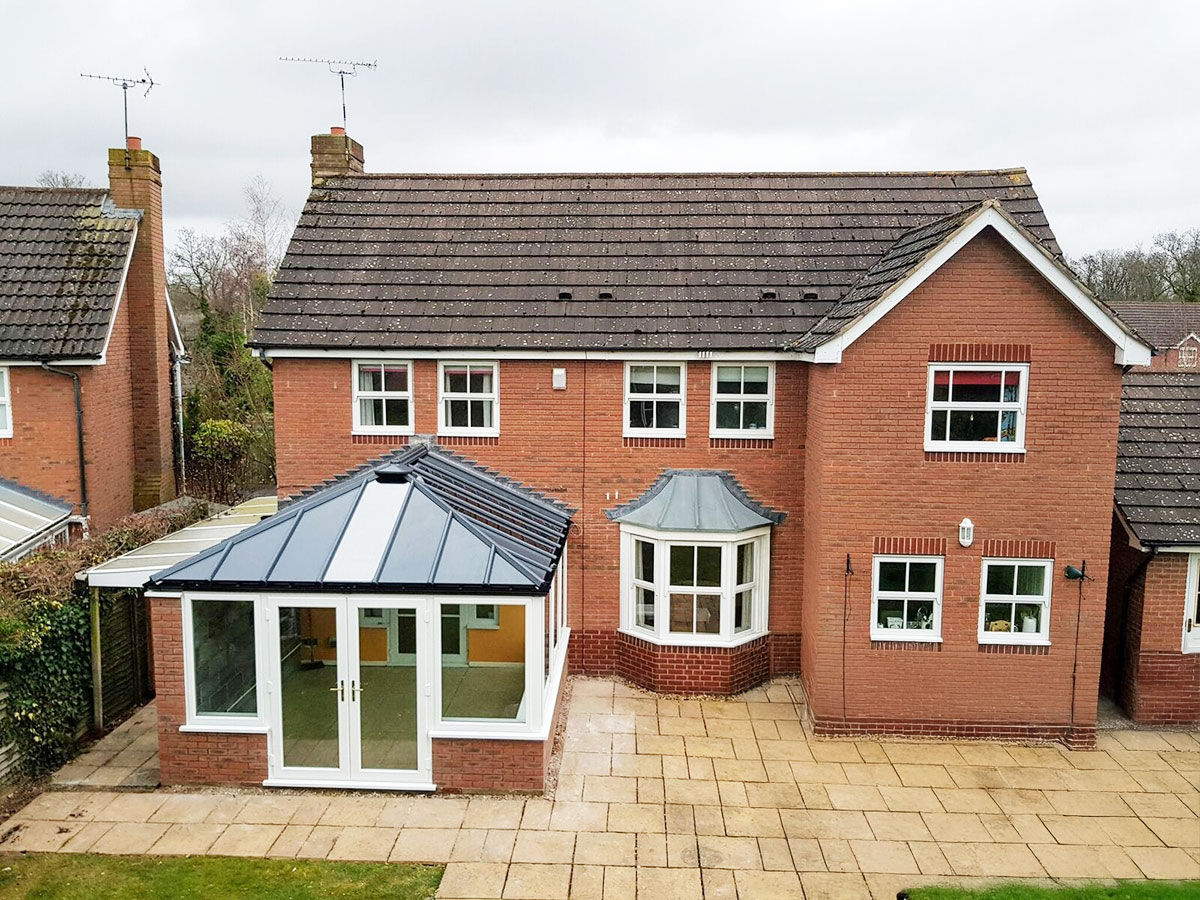 Red brick house with a newly installed conservatory featuring a dark grey solid roof and white double-glazed doors and windows