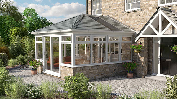 Edwardian-style cream conservatory attached to a stone house with a tiled roof and garden