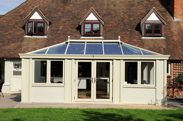 Cream conservatory with a glass roof attached to a traditional brick house with dormer windows