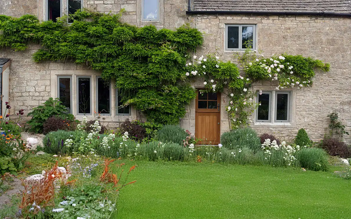 Stone cottage with timber door and heritage-style windows surrounded by a lush garden.