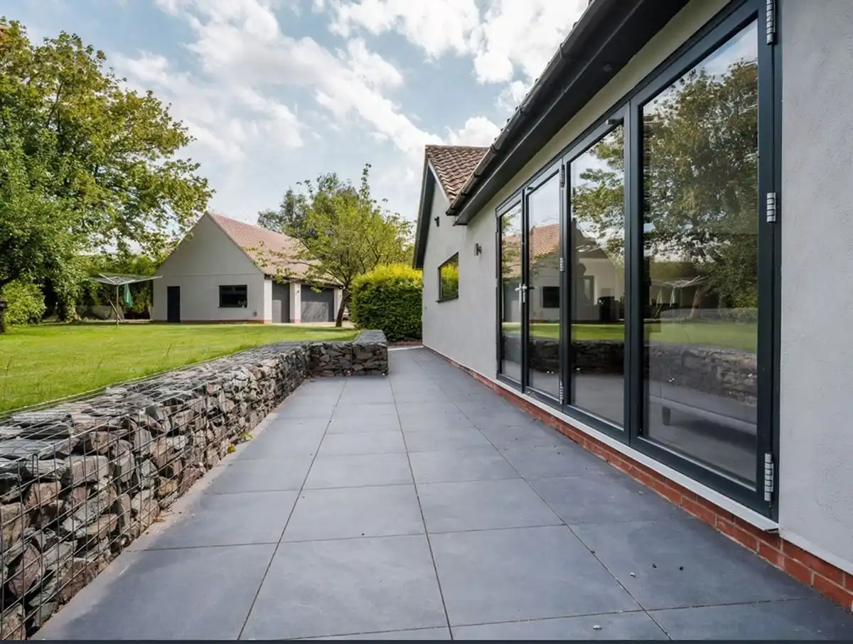 Modern home with large black-framed bifold doors opening onto a spacious patio and garden.
