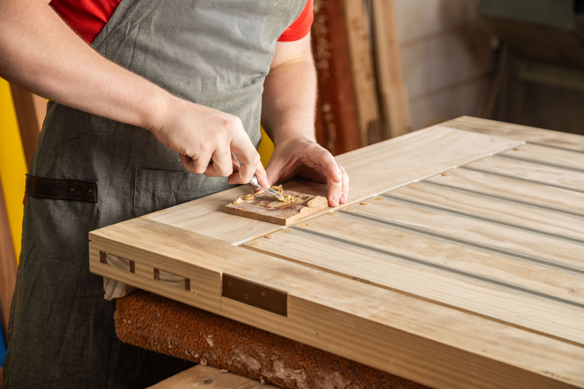 Craftsman using a chisel to shape a wooden door in a joinery workshop