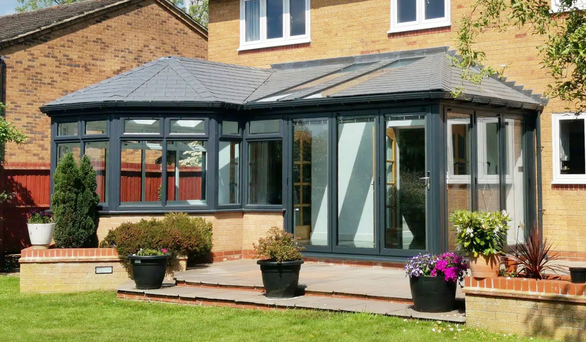 Modern conservatory with grey frames, tiled roof, and glass panels extending from a light brick home