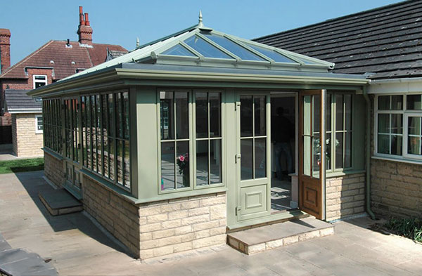 Green-painted orangery with a glass roof and stone base attached to a bungalow-style house