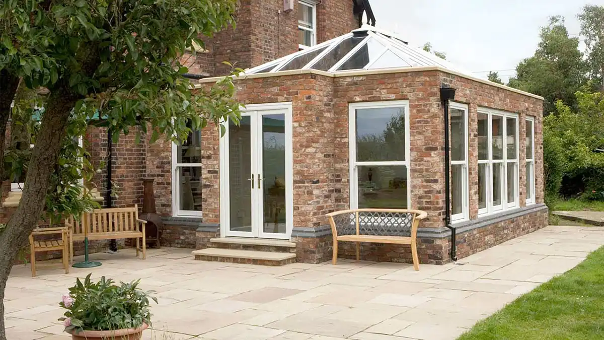 Cream-finished orangery extension with glass roof and French doors on a brick home.