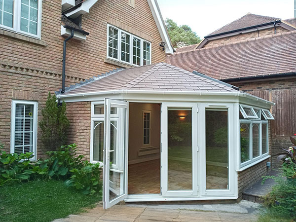 Cream conservatory with tiled roof and glass doors attached to a modern brick house