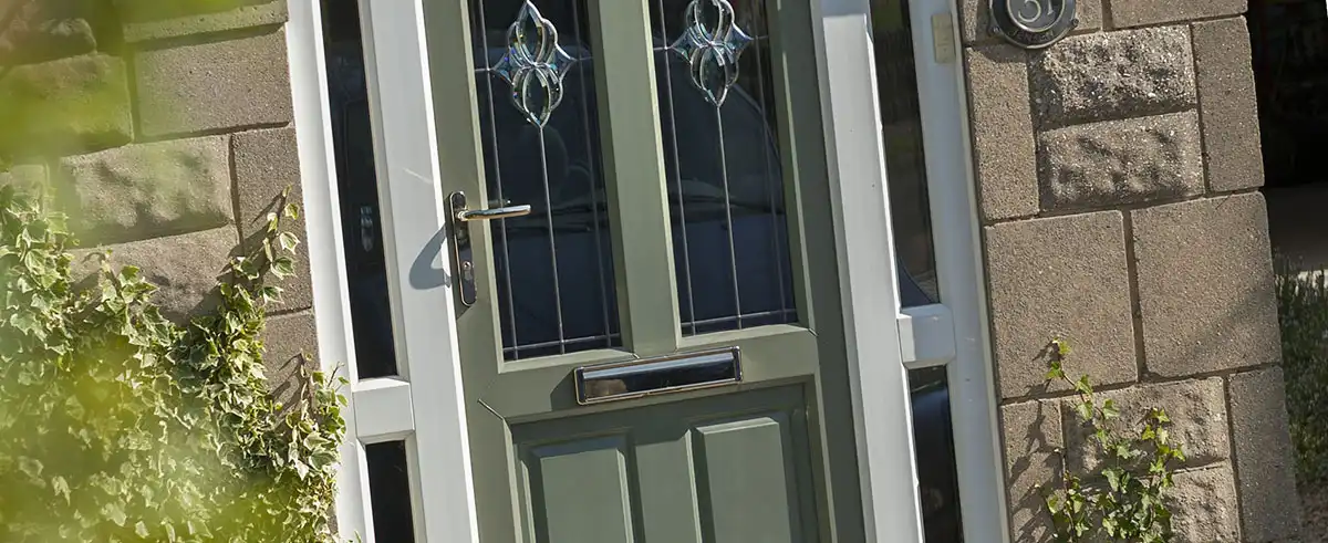 Green uPVC front door with decorative glass panels and chrome handle, framed by stone and ivy.