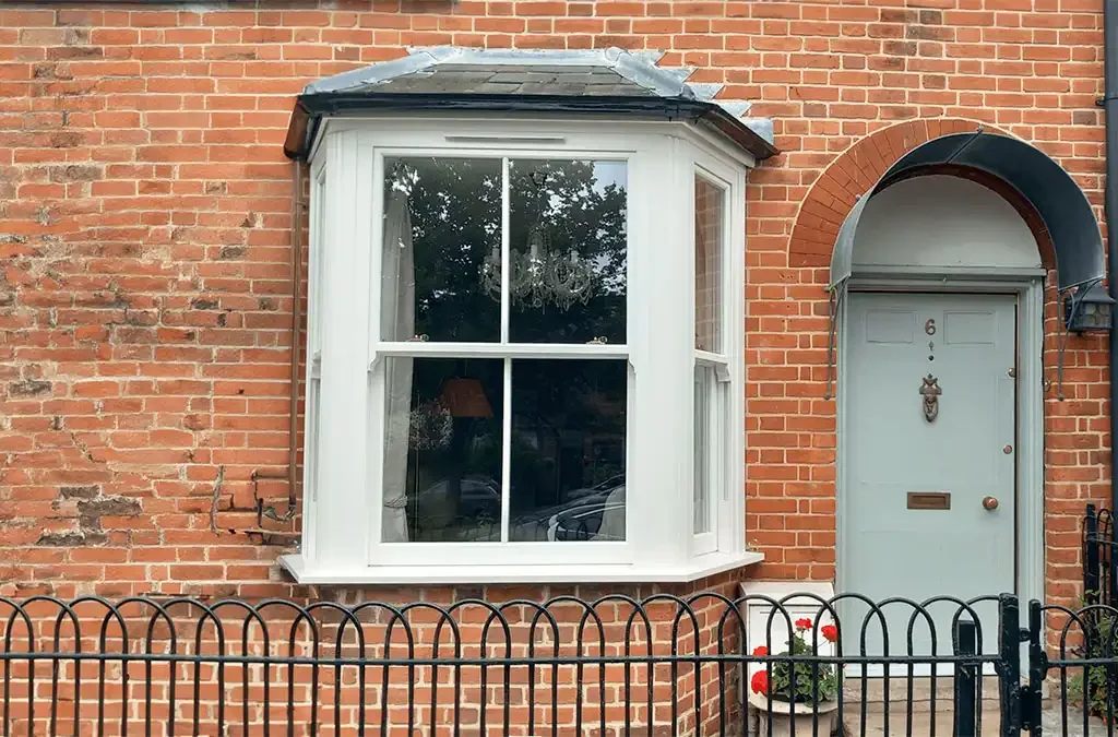 White vertical sliding bay window on a red brick house next to a pale blue door.