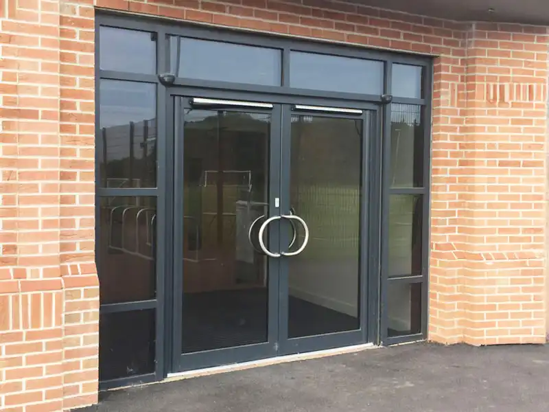 Modern aluminium commercial entrance with glass double doors and large circular handles.