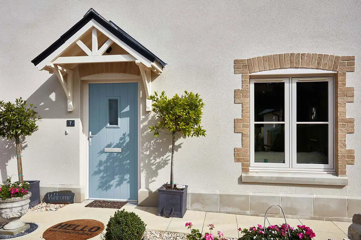 Light blue composite front door with decorative canopy next to a white uPVC flush window framed in brick