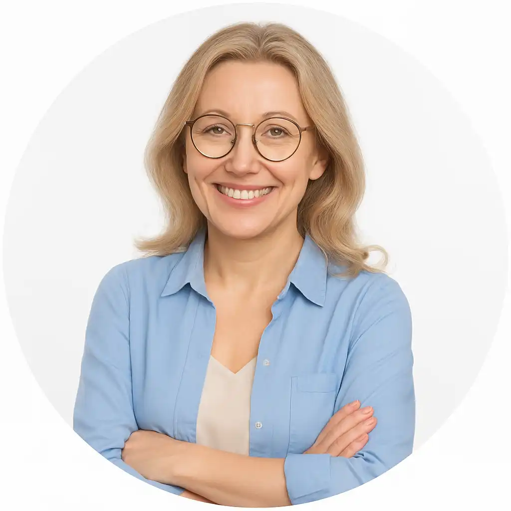 Smiling woman with blonde hair and glasses wearing a blue shirt against a neutral background.